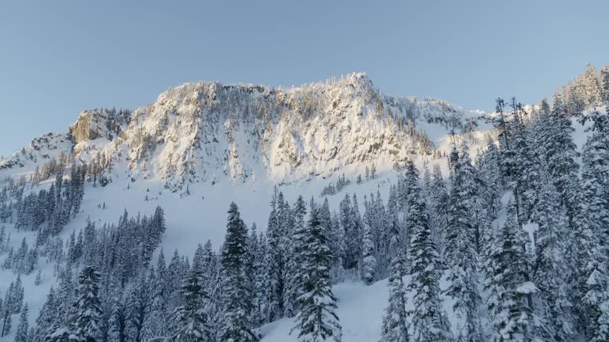 Reveal of fresh snow covering a mountain top cliff at sunrise