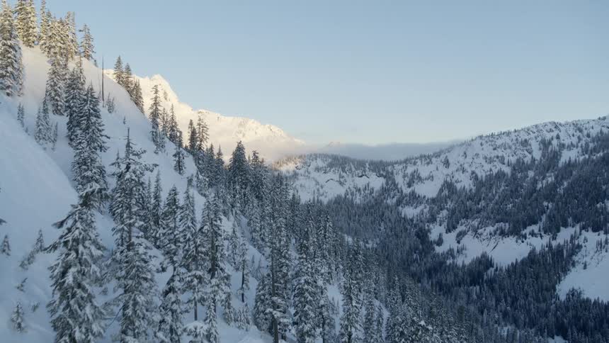 Flying along a steep slope to reveal a jagged sunlit mountaintop in the distance