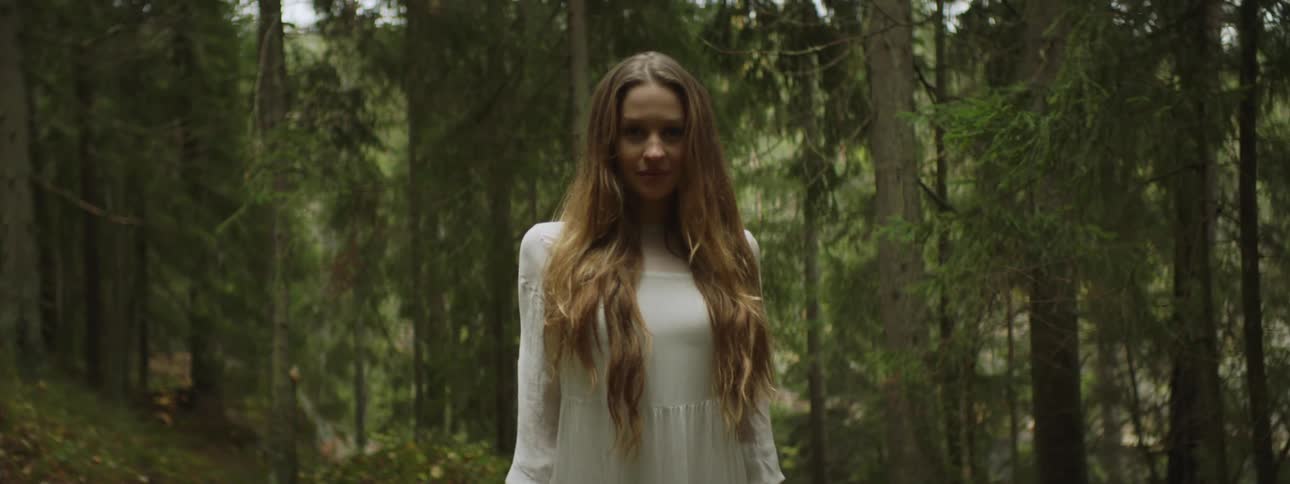 Woman with long hair wearing a white dress standing in middle of forest