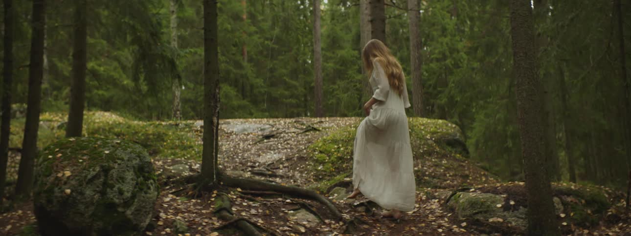 A woman in a long white dress walks through a forest