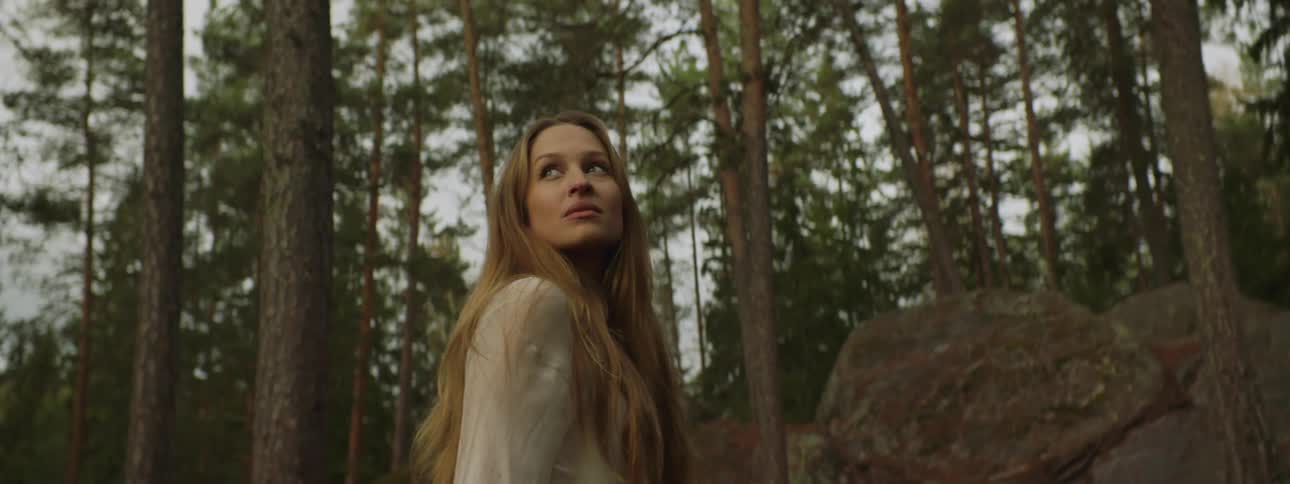 Long haired woman in white dress stands in the forest