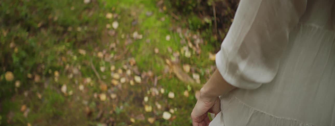 A white woman in a dress walks over grass