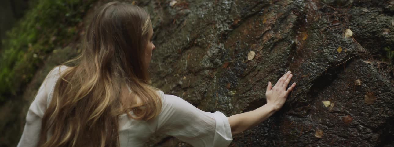 A woman is touching a rock outdoors