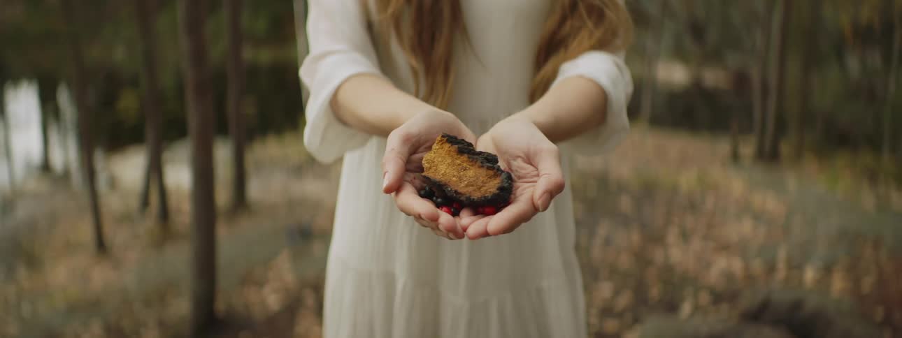 A white woman in a forest extends her hands with an offering