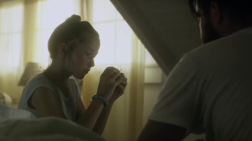 A girl sits on a bed while examining a trinket