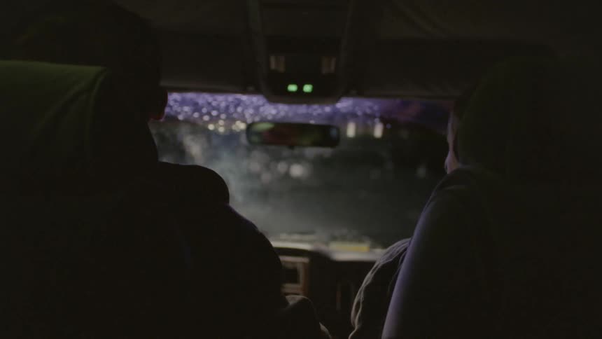 Two people are sitting in a car one lights a cigarette