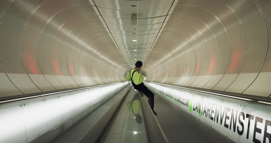 A teenager sits on a railing in a tunnel and then jumps off