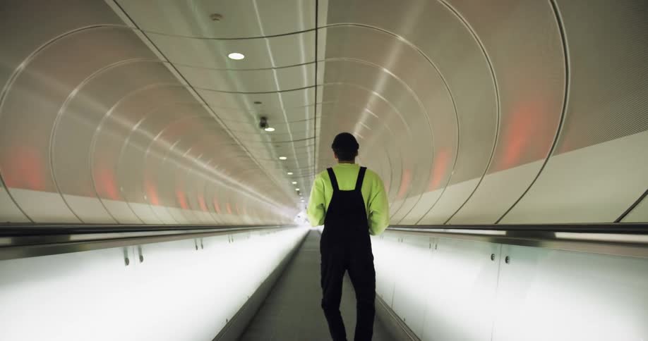 A man is dancing to his music as he rides a moving sidewalk