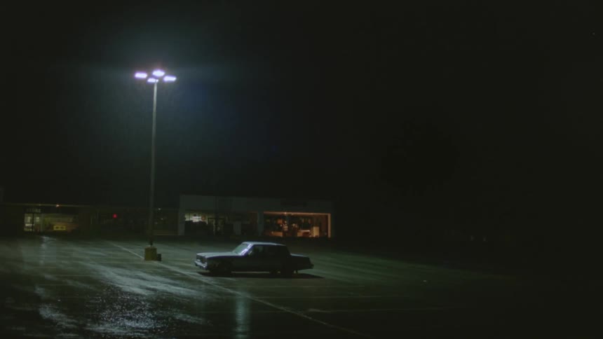 A lone vehicle in a parking lot at night during a rainstorm