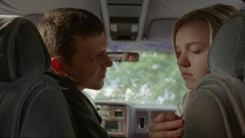 A man kisses a woman in the passenger seat of a parked car