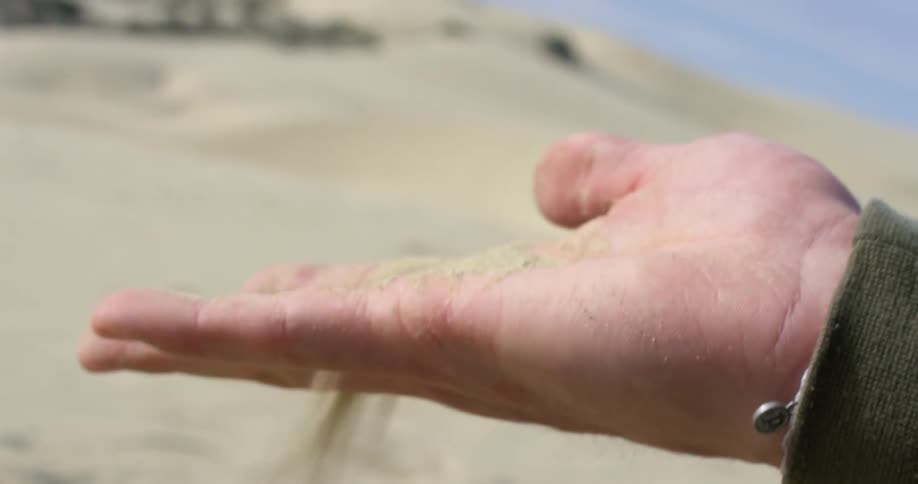 Man picks up sand from a beach and sift it through his fingers