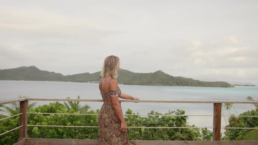 Blonde woman standing outdoors on patio looking out to the coast