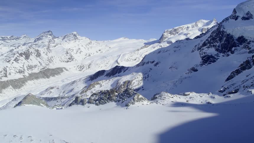 Snow covers a jagged rocky mountain slope on a bright blue sky day