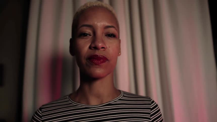 A black woman stands in front of a curtains
