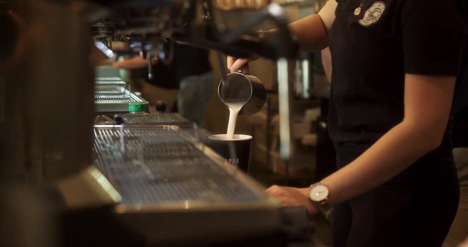 A young girl makes a latte in a coffee shop