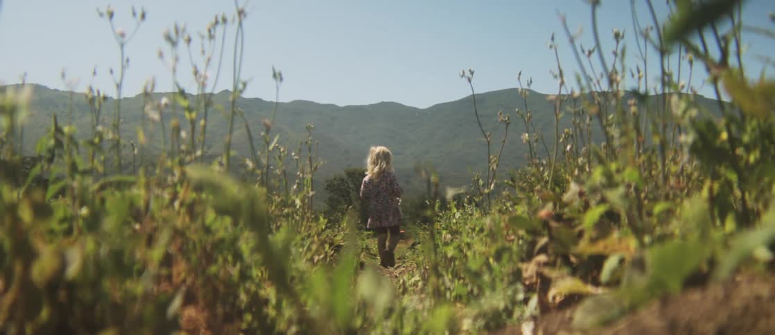 A girl is carrying a bucket as she walks over a field