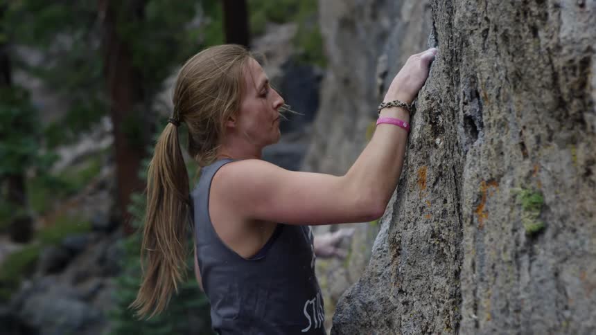 Woman rock climbing stops to powder her hands with talcum