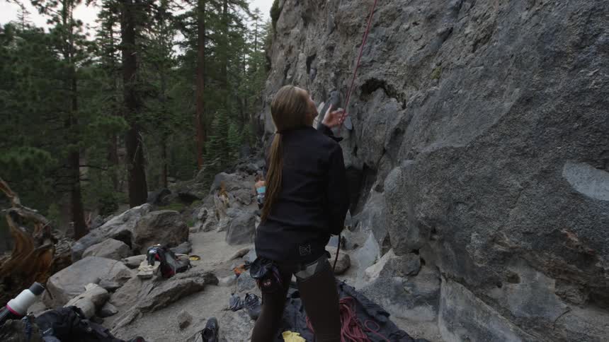 A female rock climber standing at the base of a rock face testing a rope in preparation for a climb