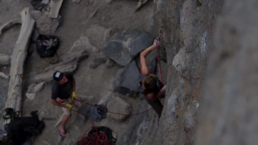 A woman climbing up a rock face secures herself while a man hold a rope below
