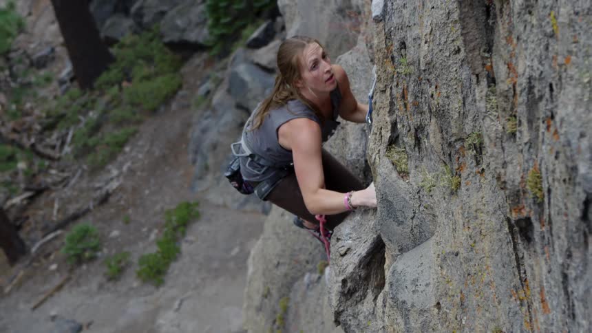 A female rock climber ascending a tall cliff in a woodland