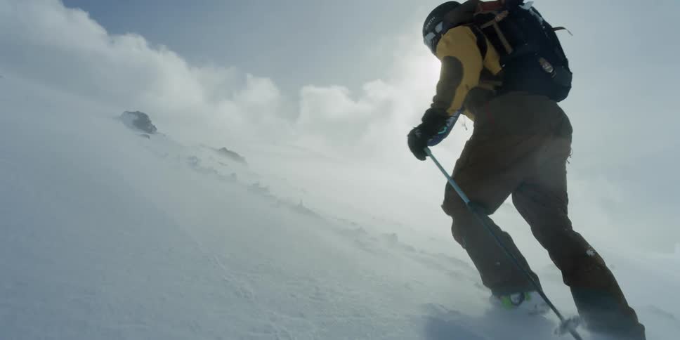 A man carries skis up a hill in a wind storm
