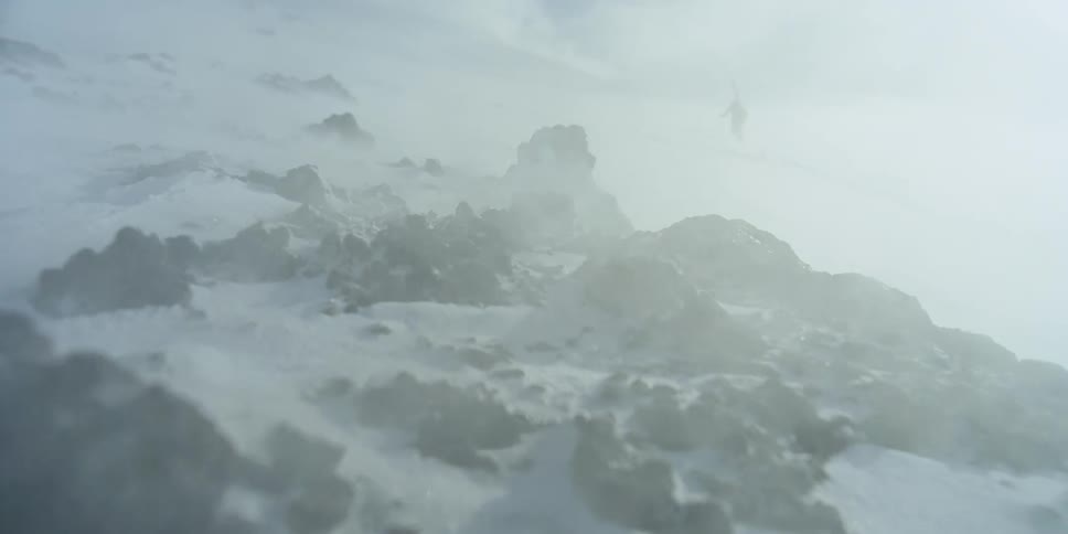 A skier walks up a mountain through intense wind