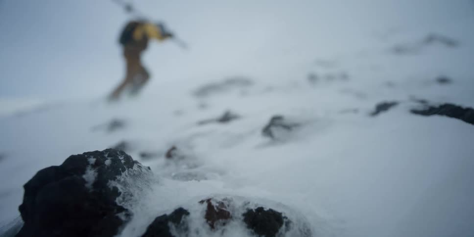 A person slowly climbs a snow covered mountain in the wind