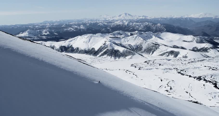 Aerial wide as a skier flies down a slope with a beautiful valley beyond