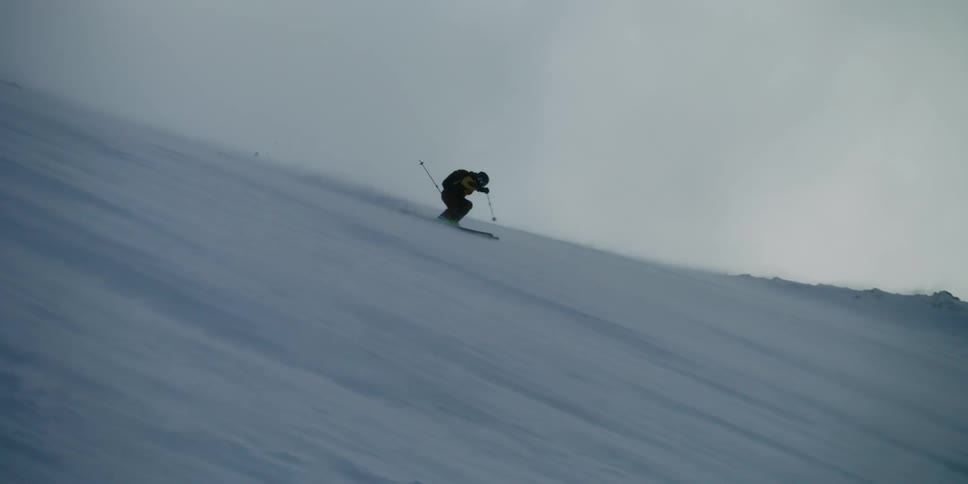 A skier glides down a windy mountain side on a cloudy day