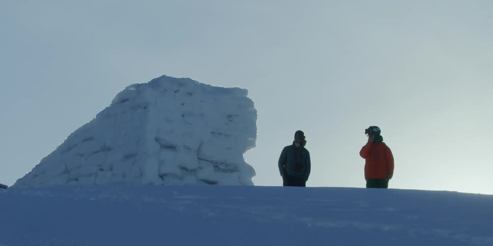 Two skiers stand by a snow jump