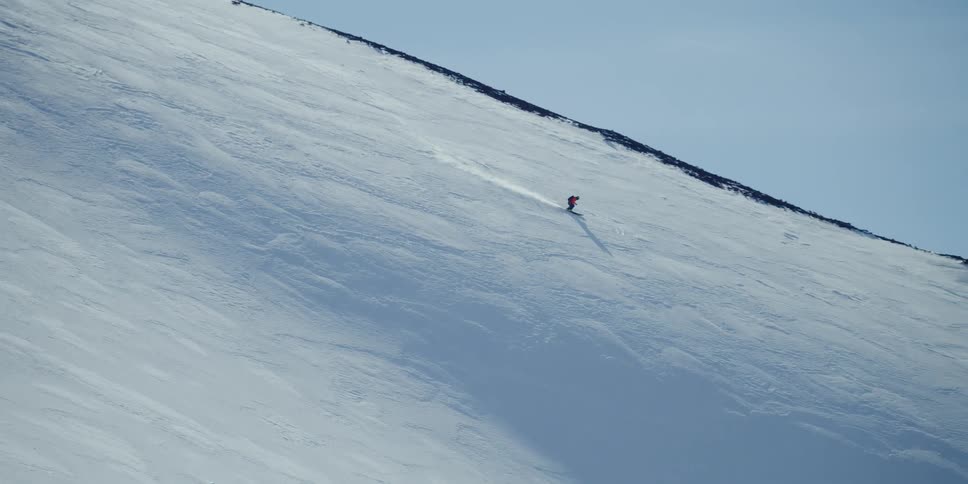 A person skis down a snowy ridge in profile