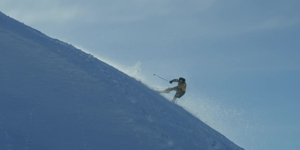 Skier falls and rolls down a ski hill under a blue sky