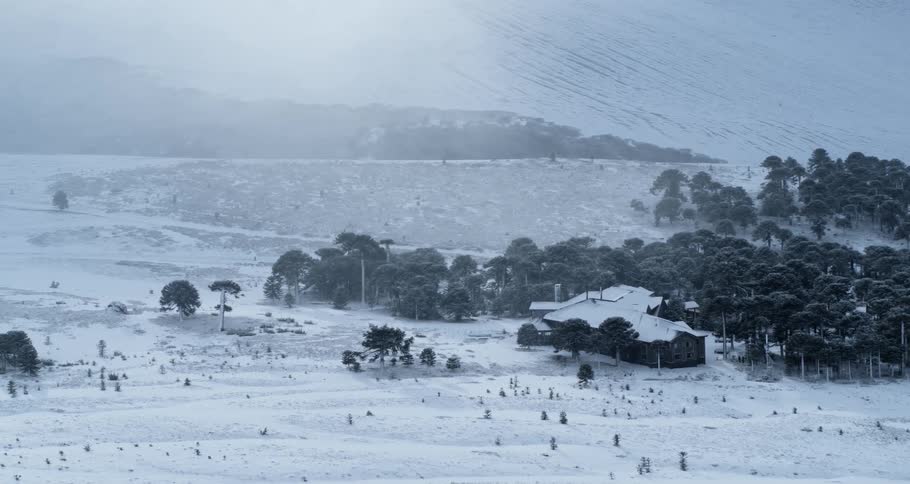 Aerial of a home in a remote rural area covered in snow near mountain at dawn