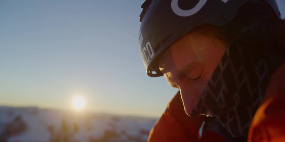 A skier puts on his helmet at sunset