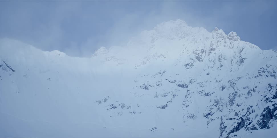 Clouds swirl around a snow covered mountain