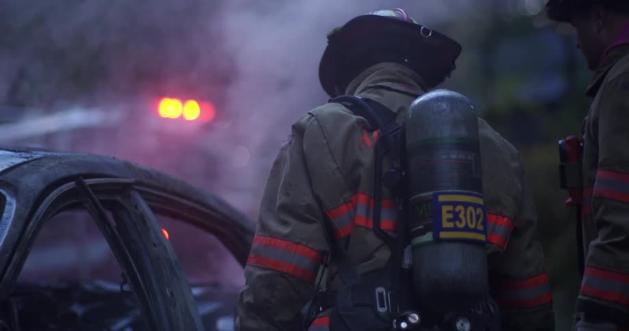Two firefighters look over a smoking and burnt car