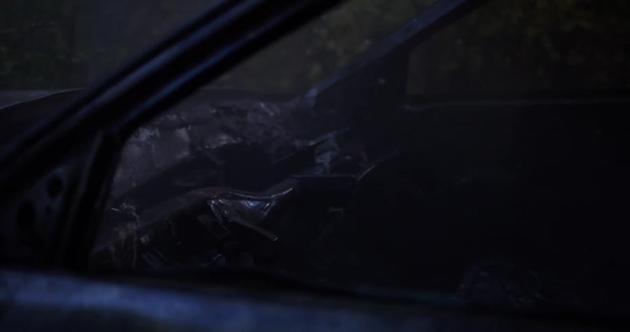 Remains of a burnt car parked outdoors with smoke still coming out