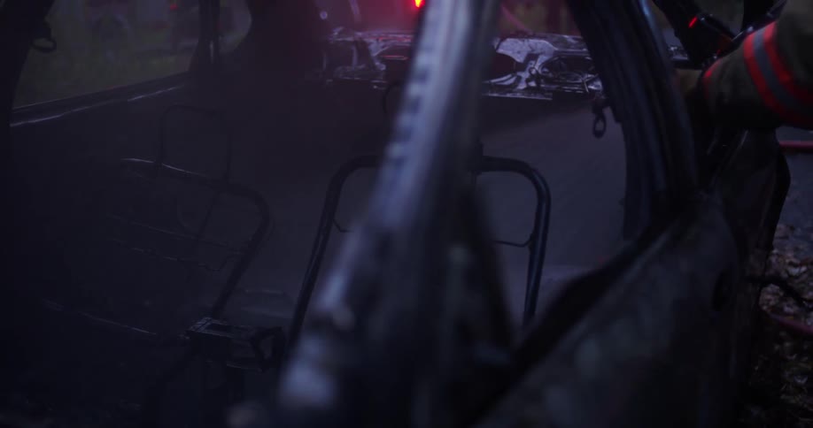 A firefighter uses a water hose on a burned vehicle