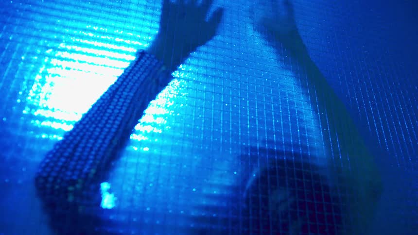 A woman dancing under a blue light behind a wall of patterned glass