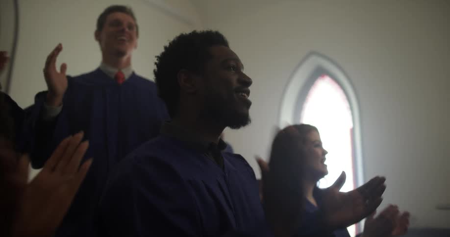 A mixed gender church choir singing and clapping their hands in a church