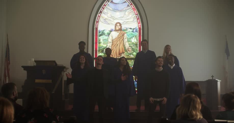 A choir singing with a stained glass window of jesus in the background