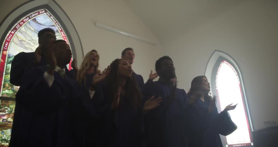Church choir claps and sings next to stained glass windows