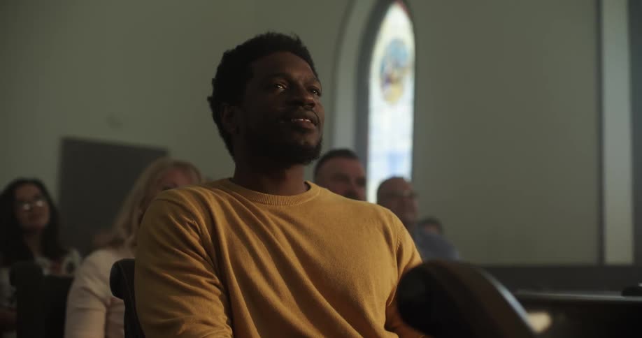 A man sitting in a church pew nods and smiles looking content