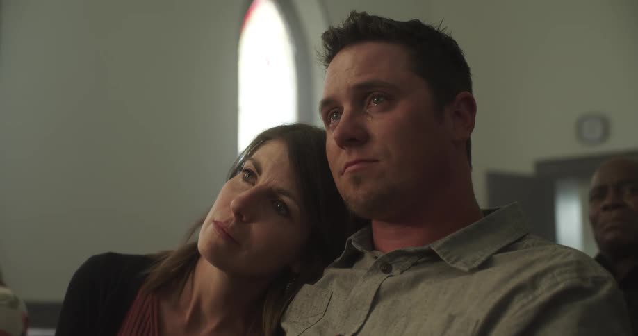 Man sitting on a pew in the church cries while his wife comforts him