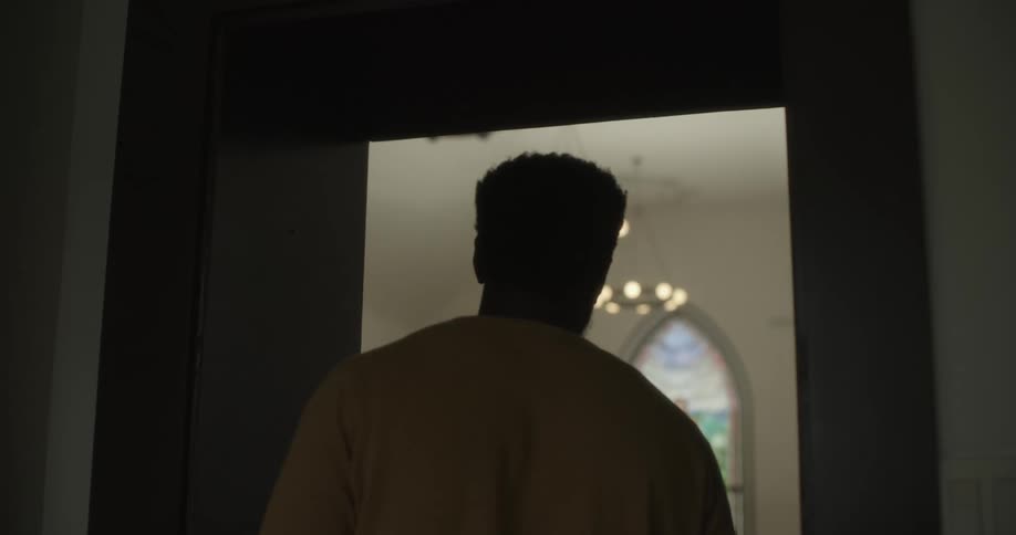A man walks up to a door and looks into a chapel with a stained glass window