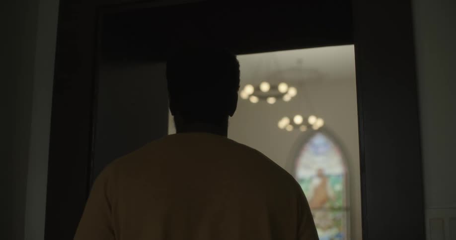 A black man looks into a chapel through a window in a door