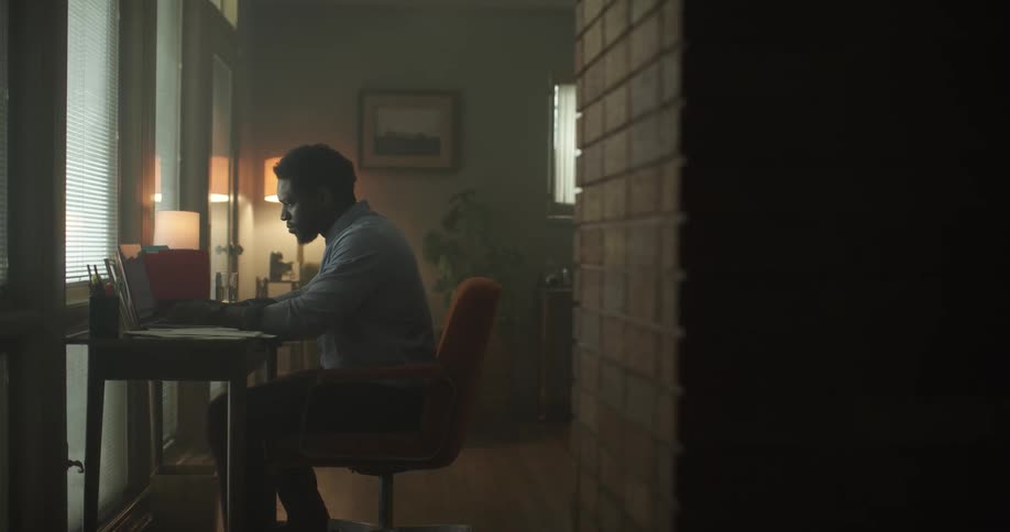 A black man sits at a table with a laptop