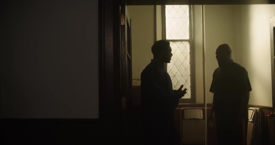 Two men stand inside and talk