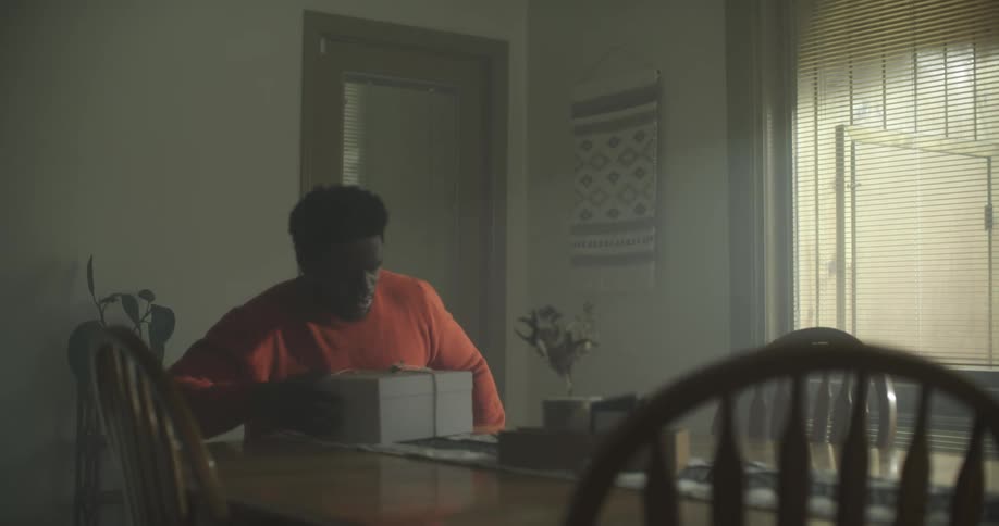 A man sitting down at a table with a box bound by string before beginning to unbind it