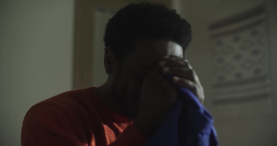 A black man holds up a shirt and laughs